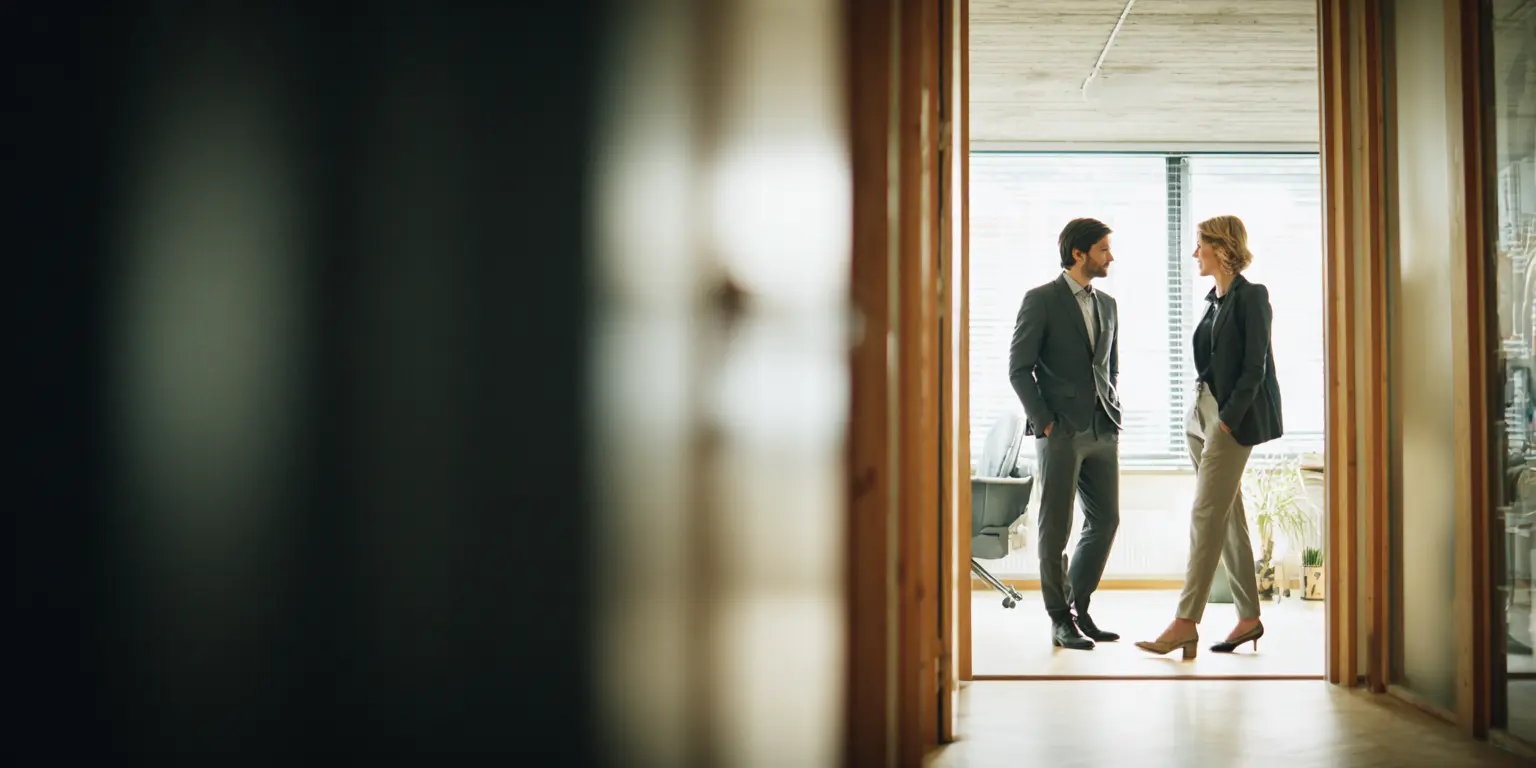 Présence humaine fonctionnelle Deux personnes échangent brièvement dans un espace de passage lors d'une visite immobilière notariale